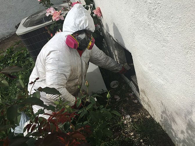 Technician in a protective suit treating an exterior wall beside an air conditioning unit